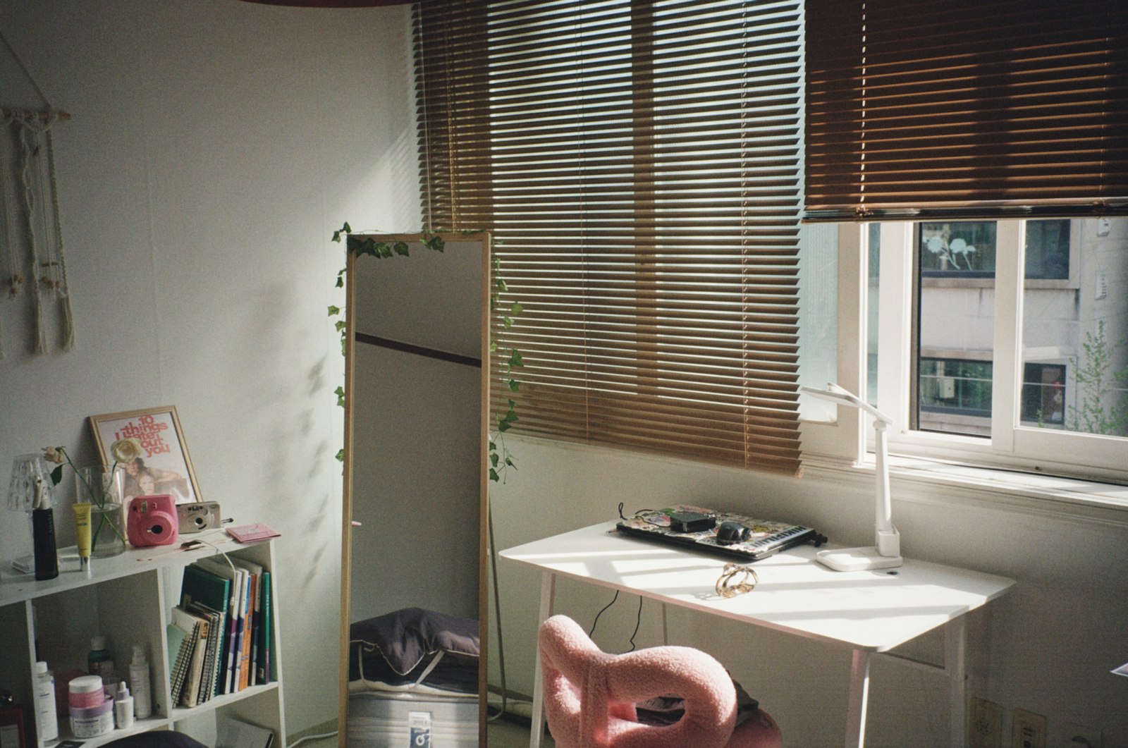 A compact study desk set against a bedroom window in a high-rise flat, blinds drawn back to a view of neighbouring blocks