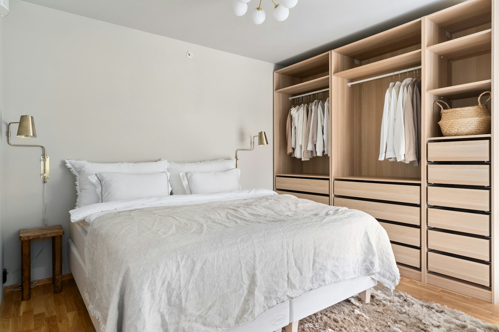 A bright bedroom with a made bed, soft throw and an open wardrobe of neatly hung clothes