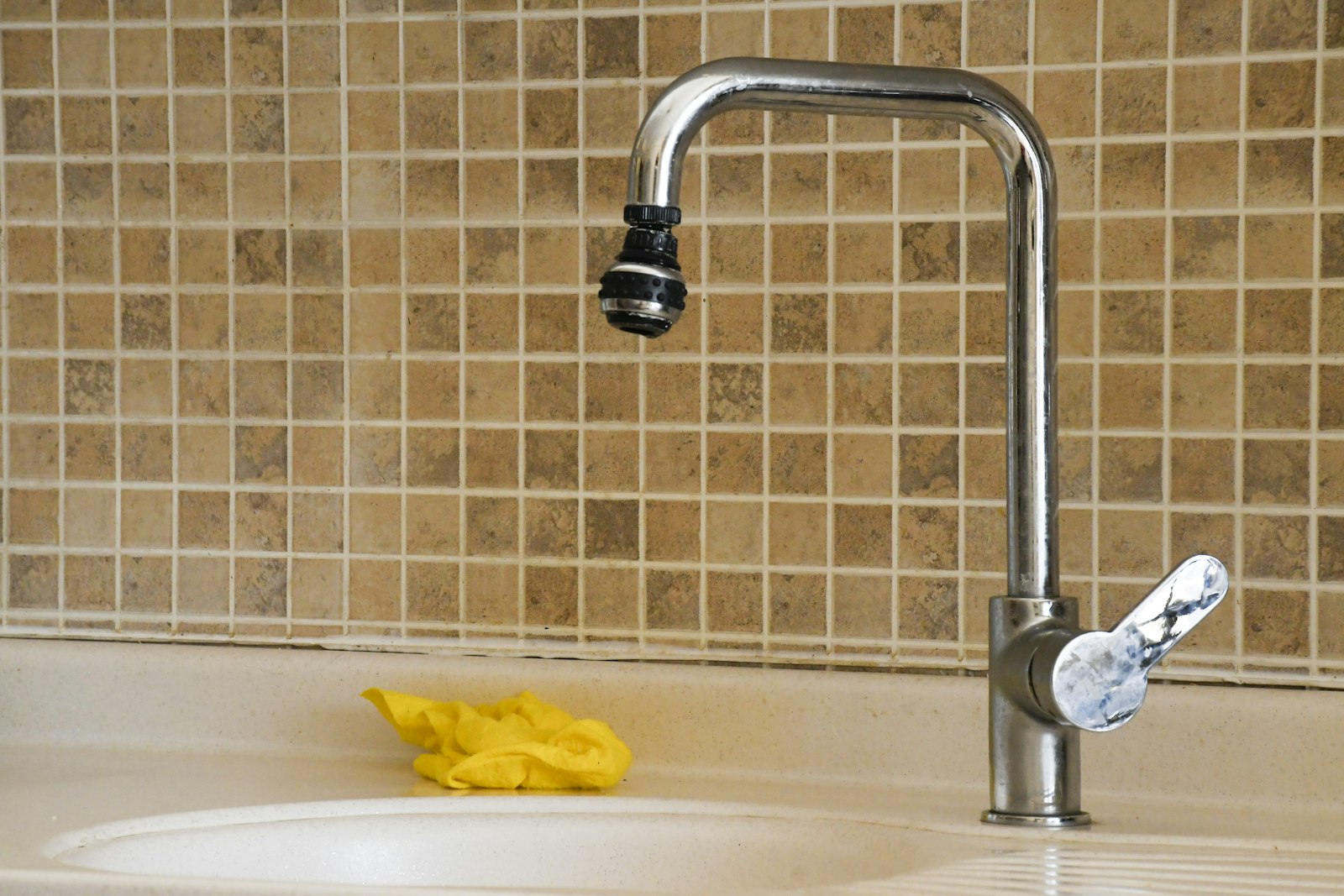 A yellow cleaning cloth resting on the edge of a sink beside a chrome tap