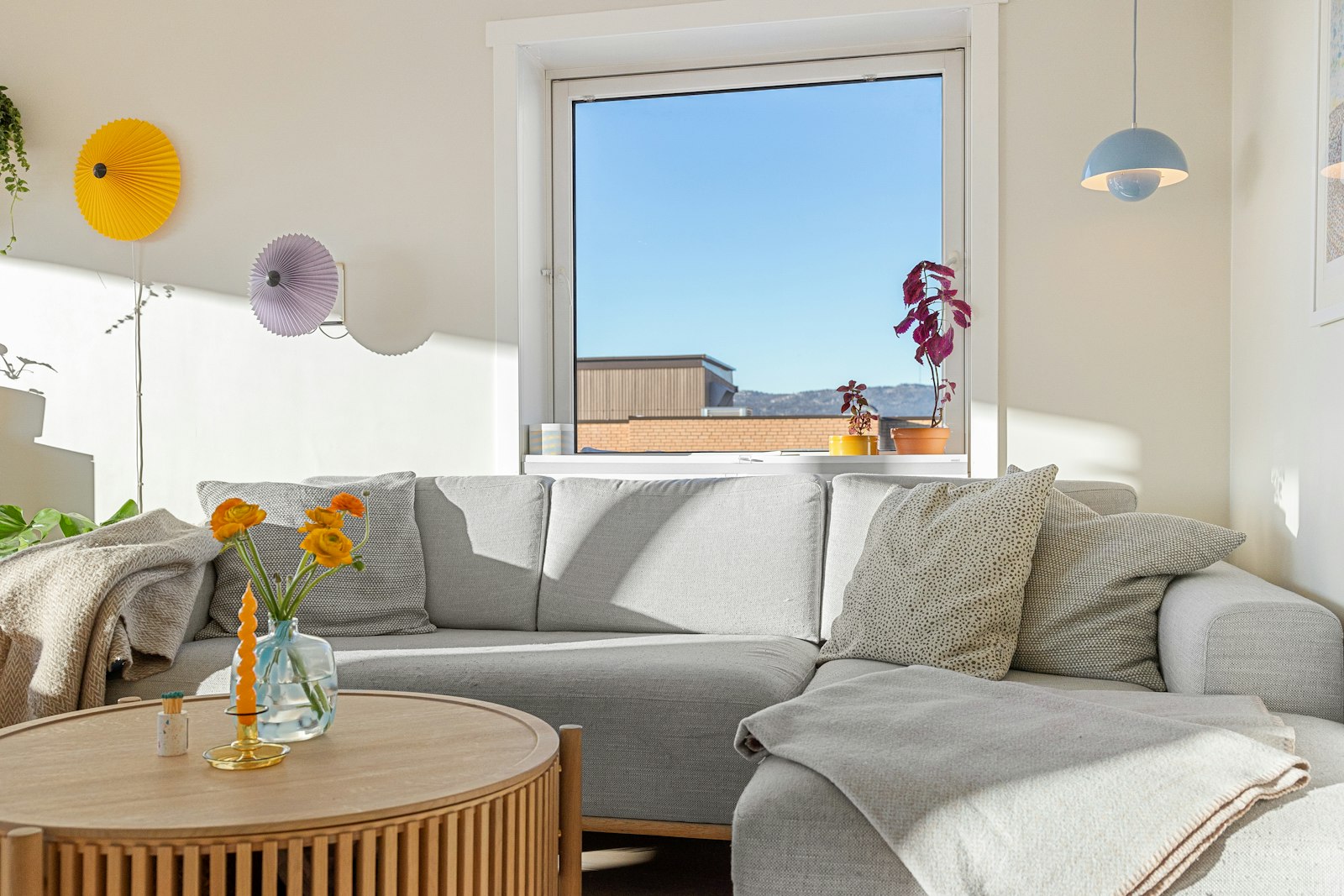 A grey fabric sofa with cushions and a folded throw beside a round wooden coffee table