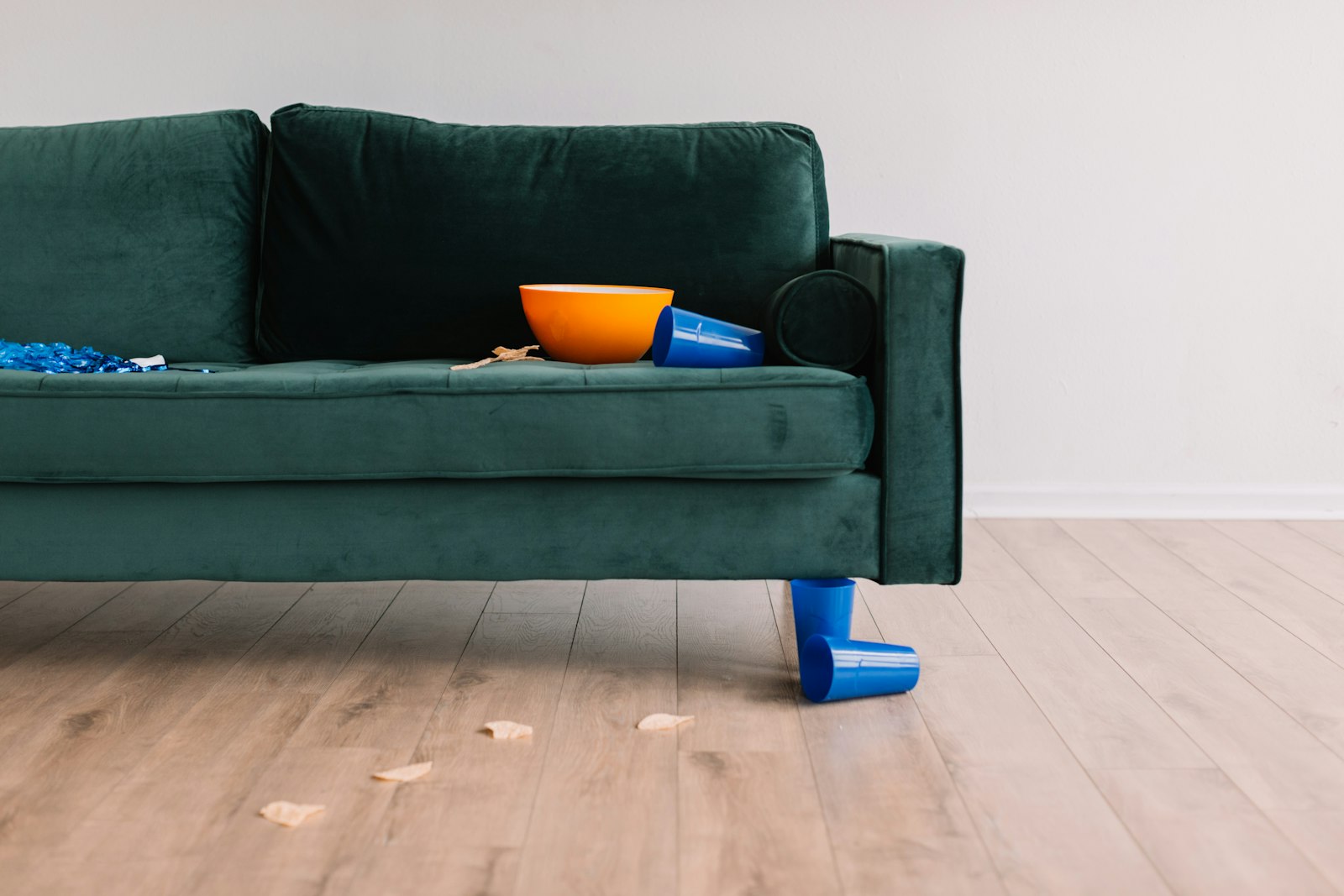 A green velvet sofa with blue toy building blocks scattered across the seat and the pale wooden floor below