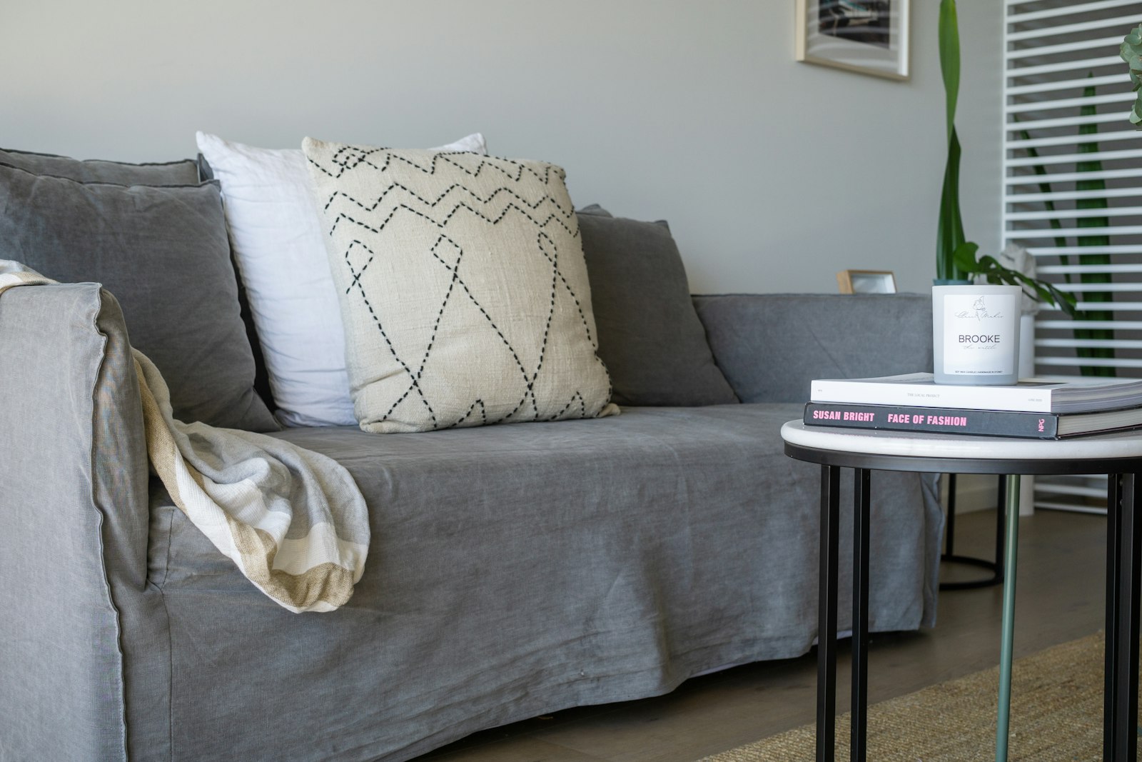 A grey linen sofa with cushions and a folded throw in a bright living room