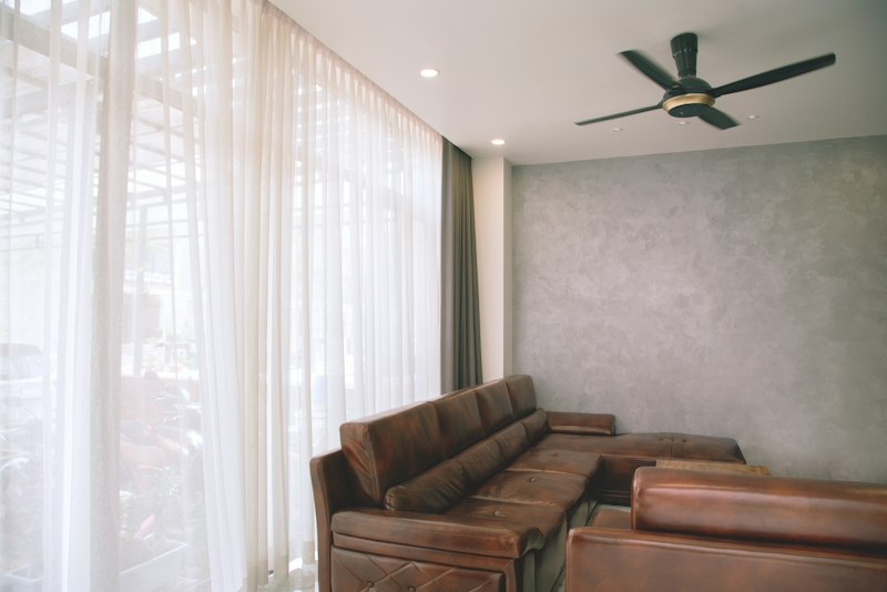 A bright living room with floor-to-ceiling sheer curtains and a ceiling fan overhead