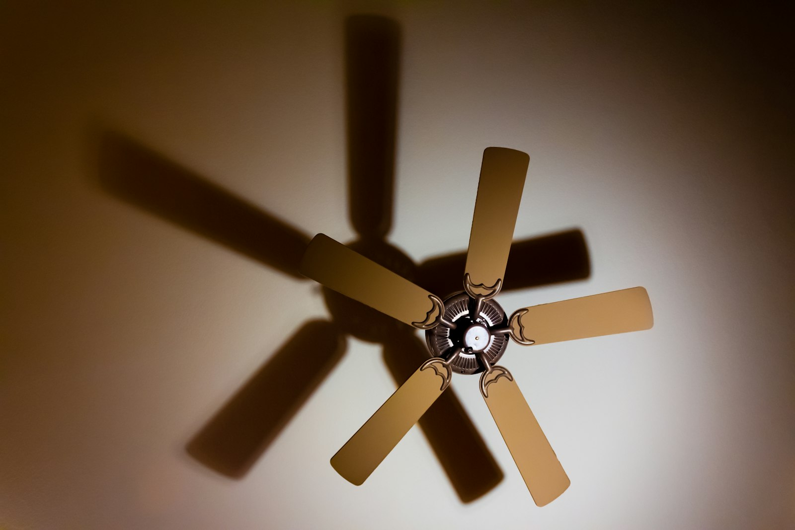 A ceiling fan turning, its blades blurred against a warmly lit ceiling