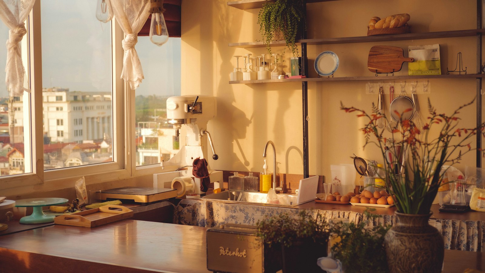 A warm, lived-in kitchen in the late afternoon, sunlight coming through the window and rooftops beyond