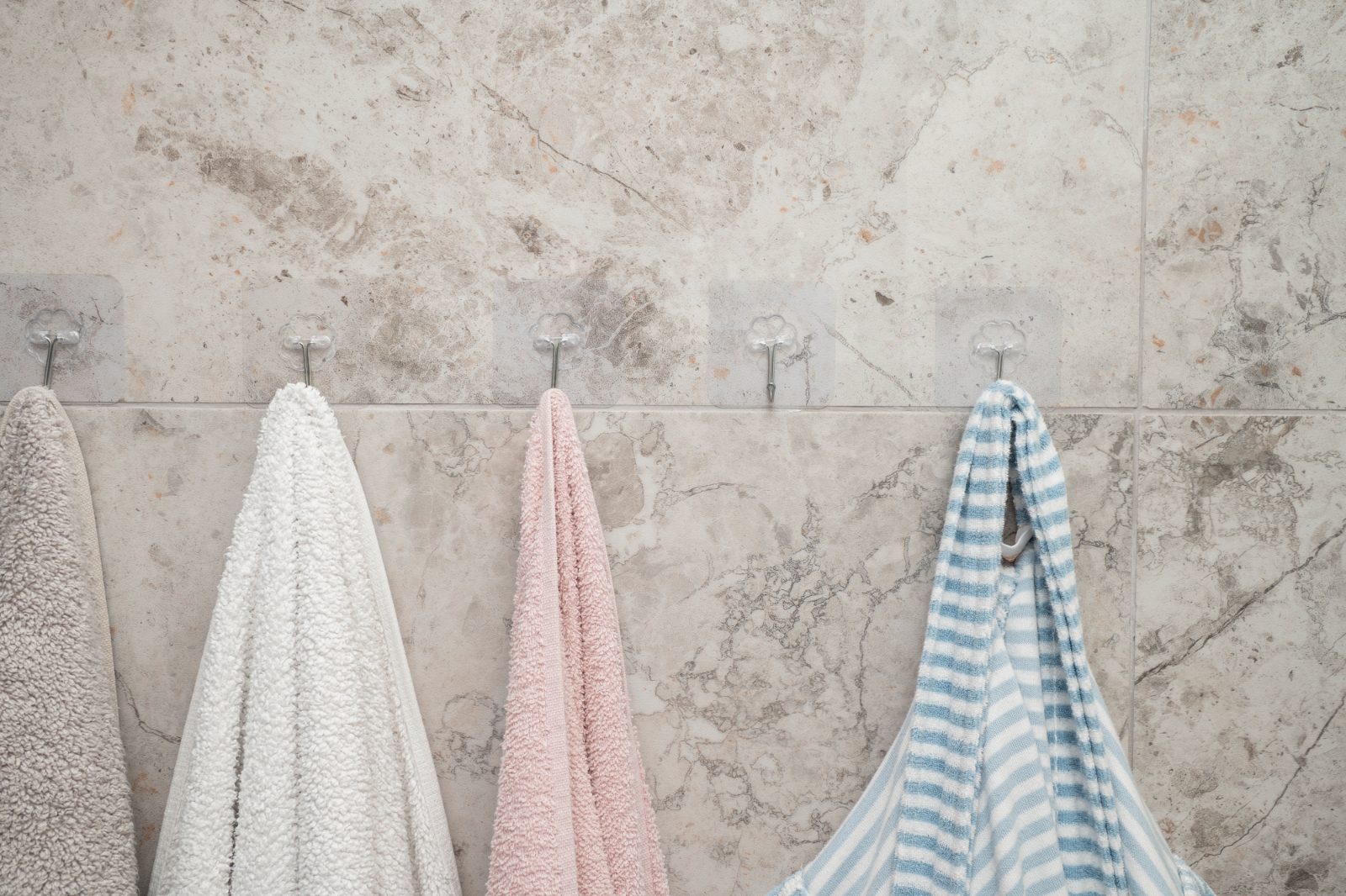 Five towels hanging on hooks along a stone bathroom wall
