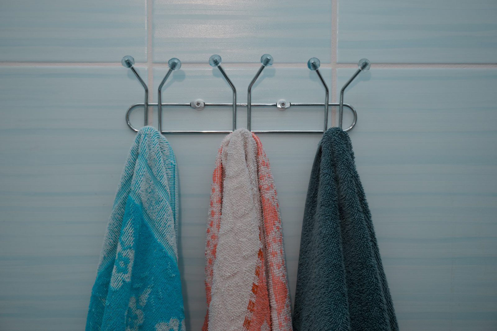 Three towels hanging close together on a row of hooks in a bathroom