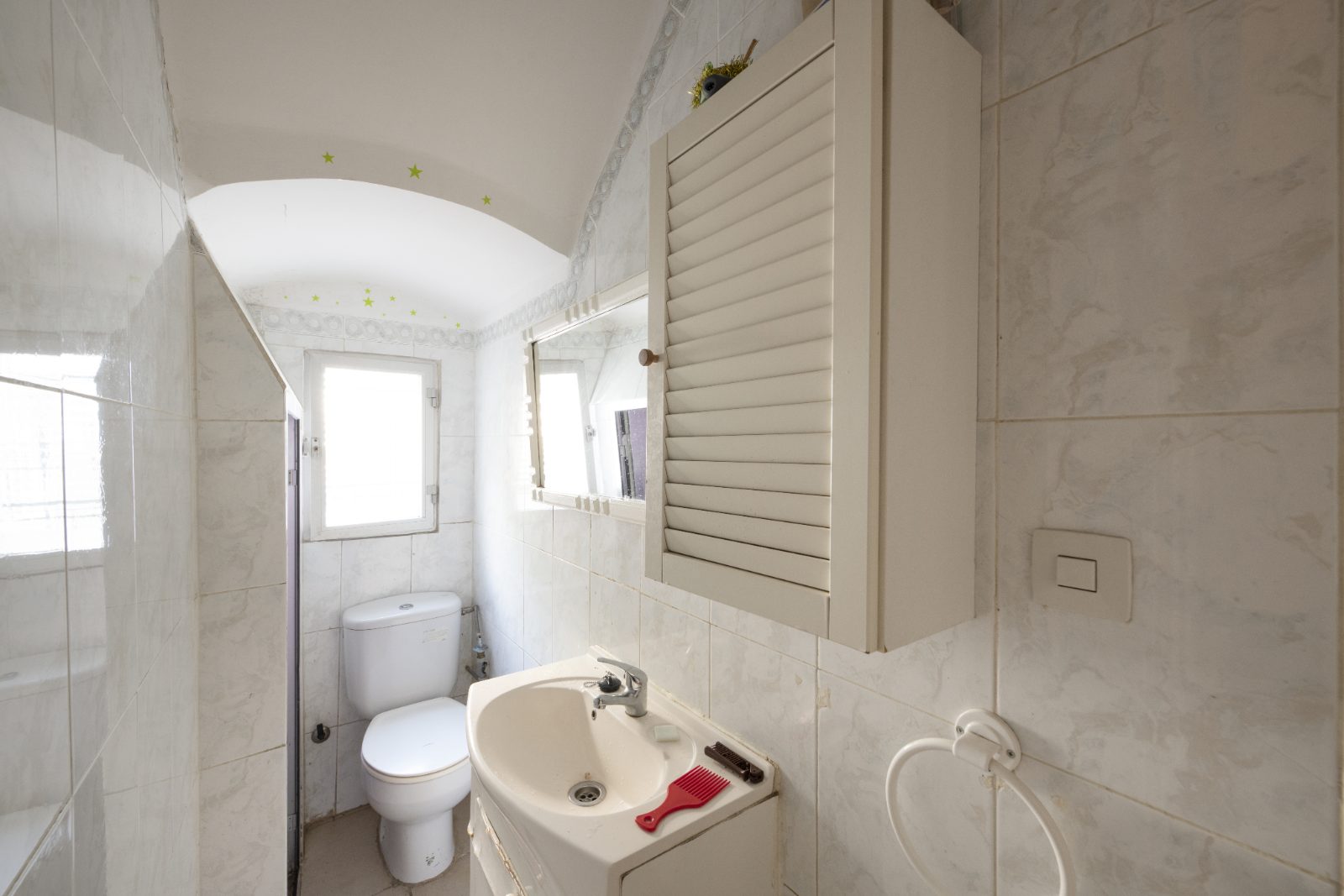 A compact bathroom with pale tiles, a basin and a floor-level shower area