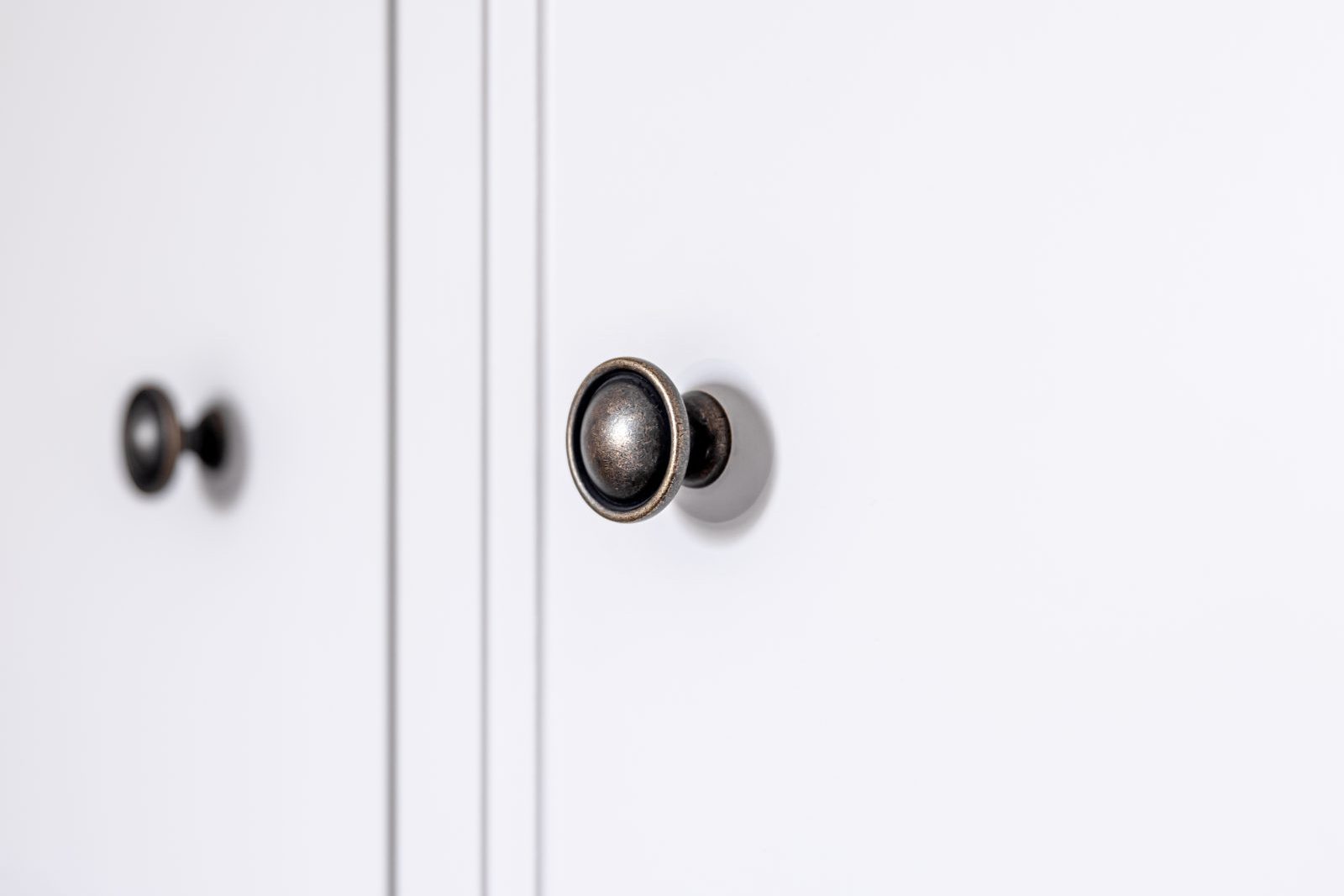 Close-up of dark metal knobs on white kitchen cabinet doors, a surface handled many times daily
