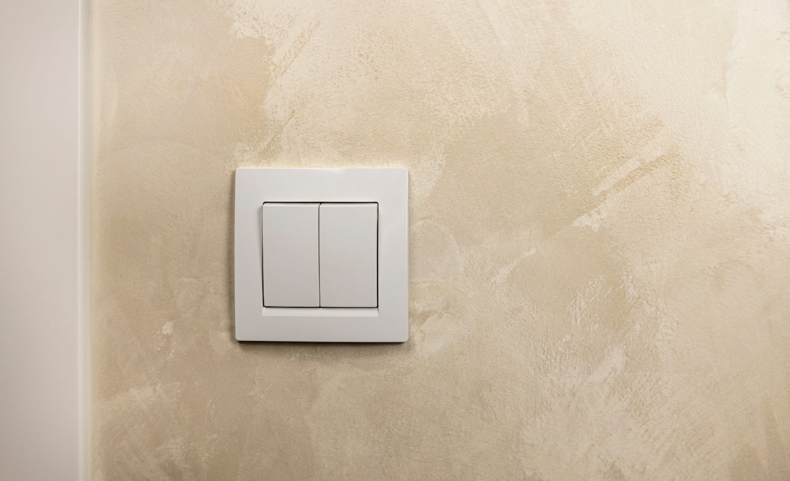 A white two-gang light switch on a textured wall, the kind pressed dozens of times a day in a Singapore flat