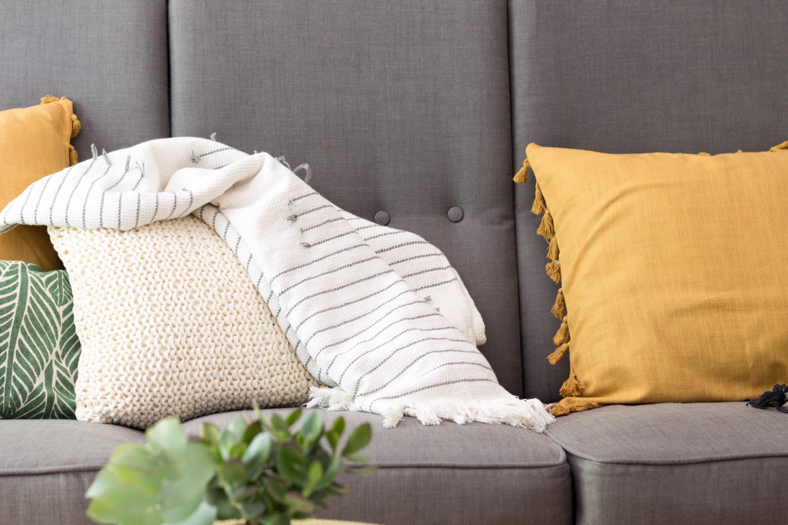 Cushions and a knitted throw on a grey fabric sofa in a bright living room