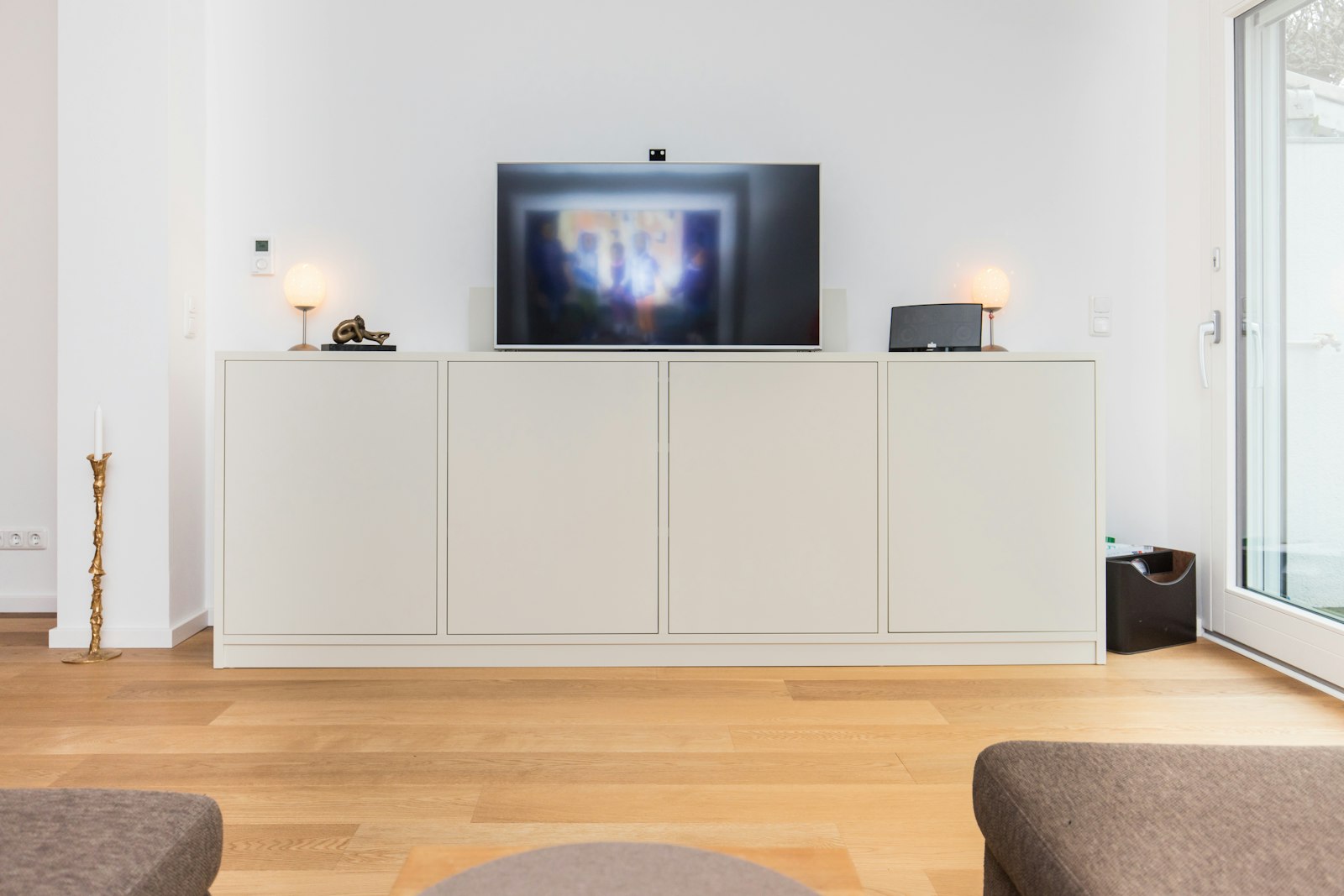 A flat-screen television switched on above a low white sideboard in a bright living room