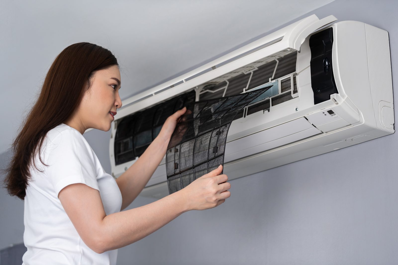 A young woman sliding the dusty filter mesh out of a wall-mounted aircon unit at home