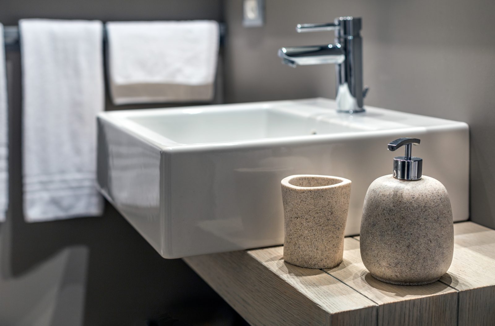 A white basin on a timber bathroom ledge with a stone tumbler and soap dispenser beside it