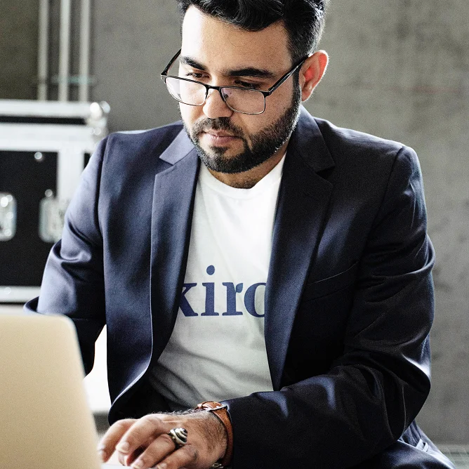 NextGen Leader Omid working on a laptop wearing a white shirt with Kiron logo