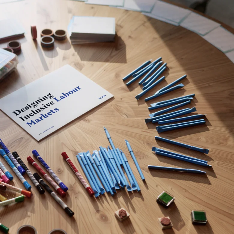 A desk with a sign stating "Designing Inclusive Labour markets" around it pens, tape and cards to brainstorm with