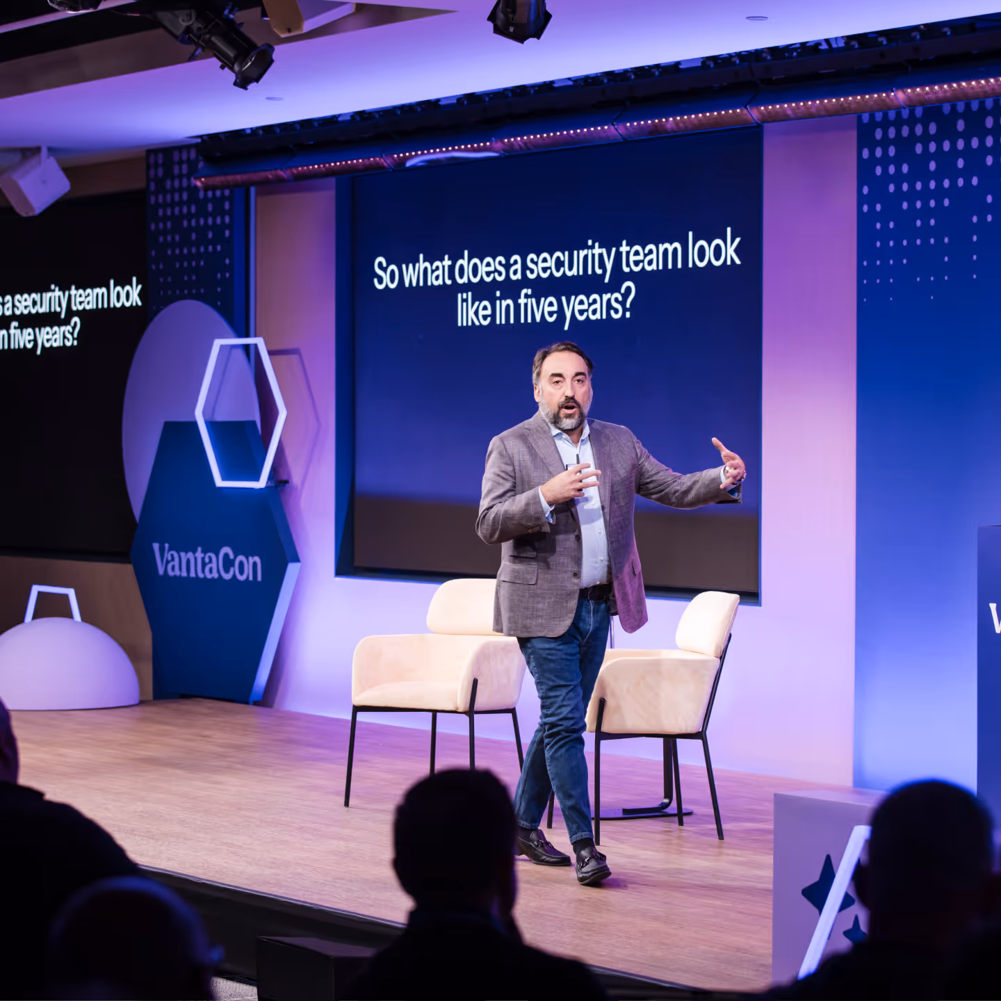 Man in a gray blazer speaking on stage during a VantaCon event with a screen behind asking, 'So what does a security team look like in five years?'