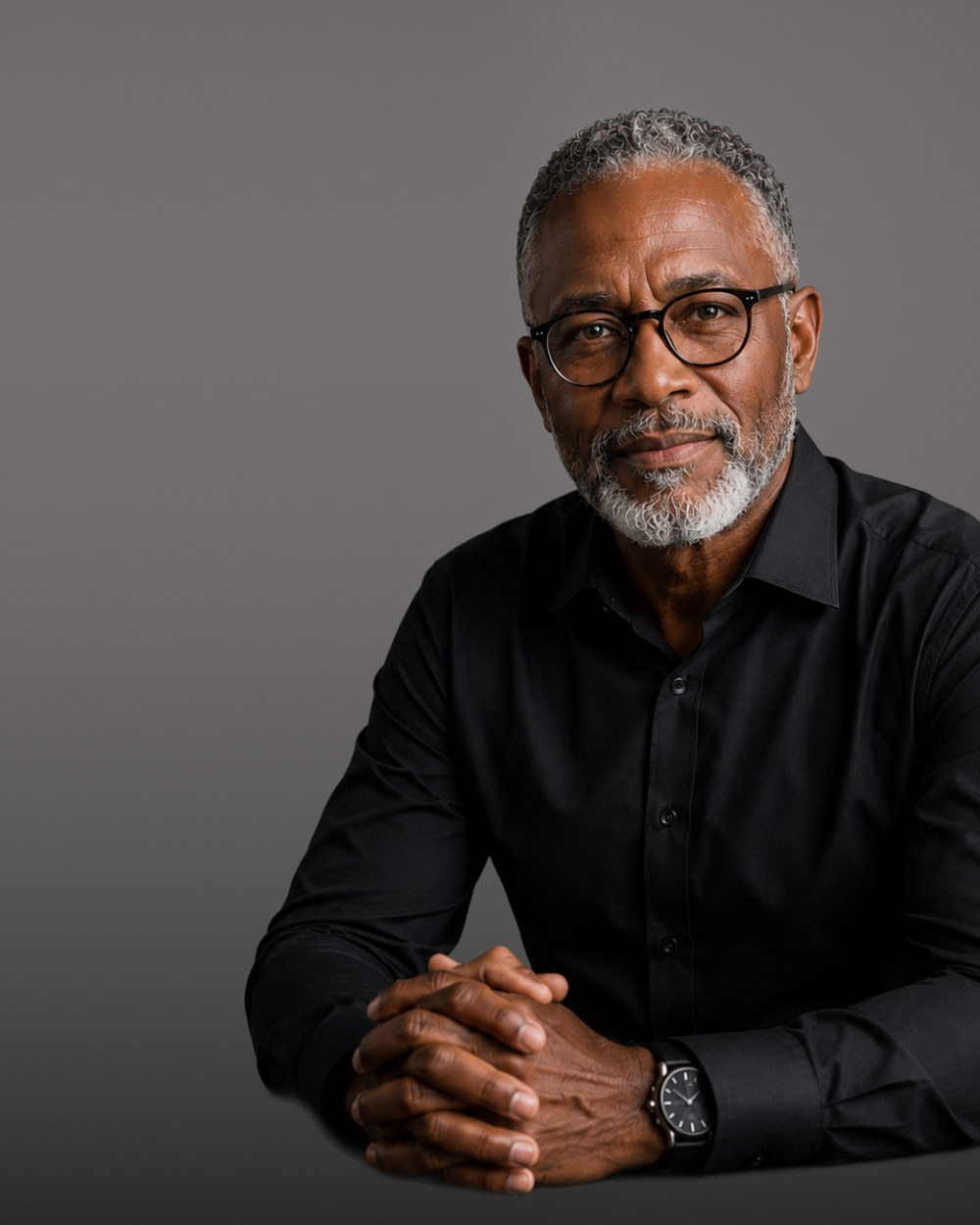 Senior professional with glasses in a black shirt, hands clasped