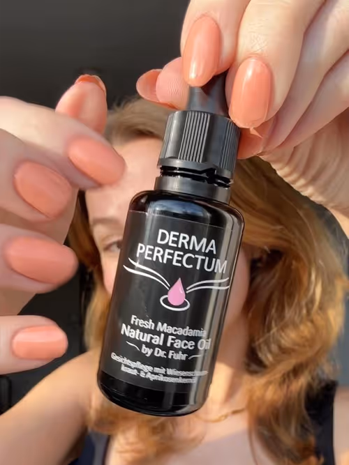 Frau mit langen, korallenfarbenen Fingernägeln hält eine Flasche Dermaperfectum© Fresh Macadamia Natural Face Oil in der Hand.