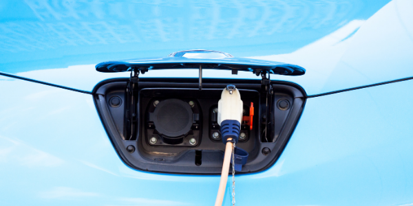 An EV charger plug inserted into a blue, light-duty electric vehicle for charging.