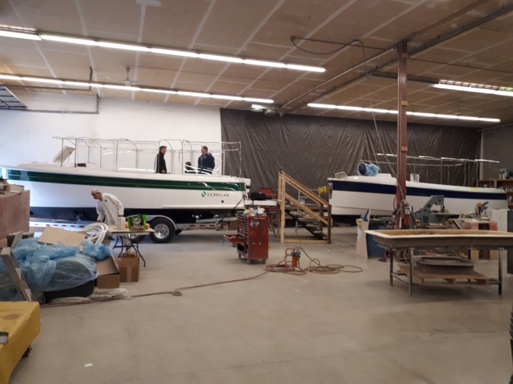 Two electric boats and a few employees at a facility of Templar Electric Boats.