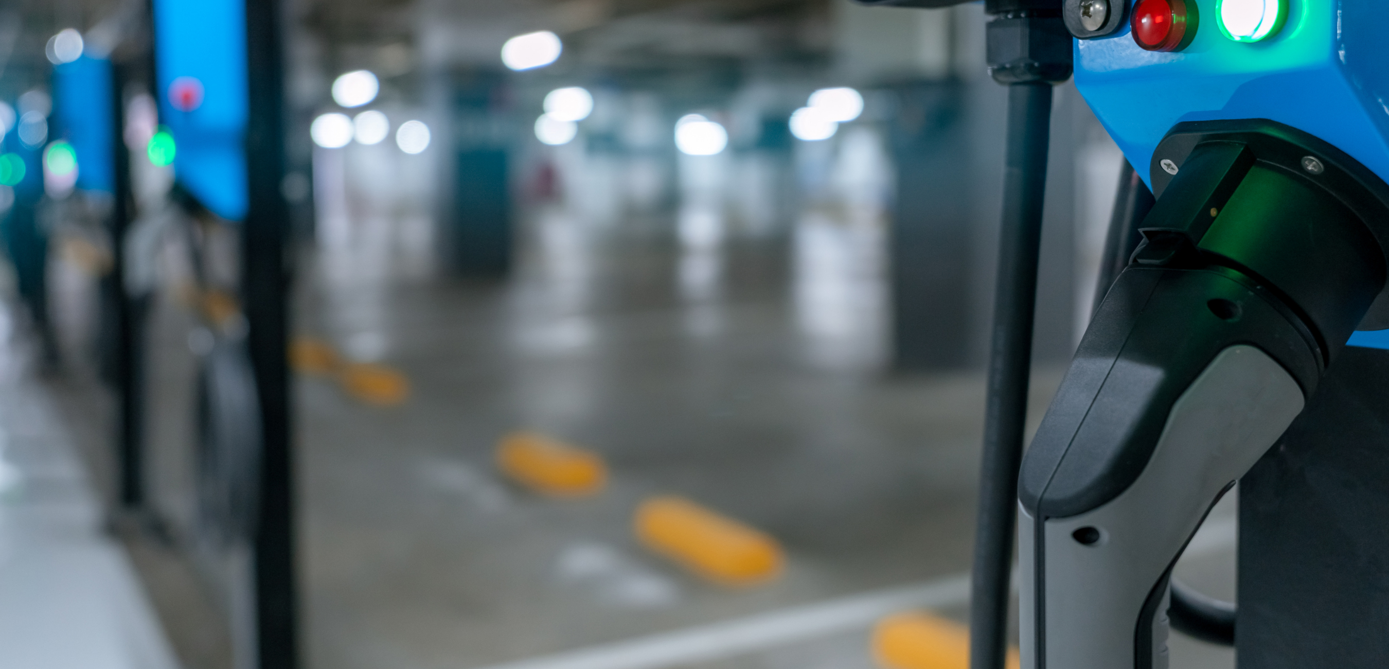Close up of EV battery plug, with blurred background showing large electric car charging station.