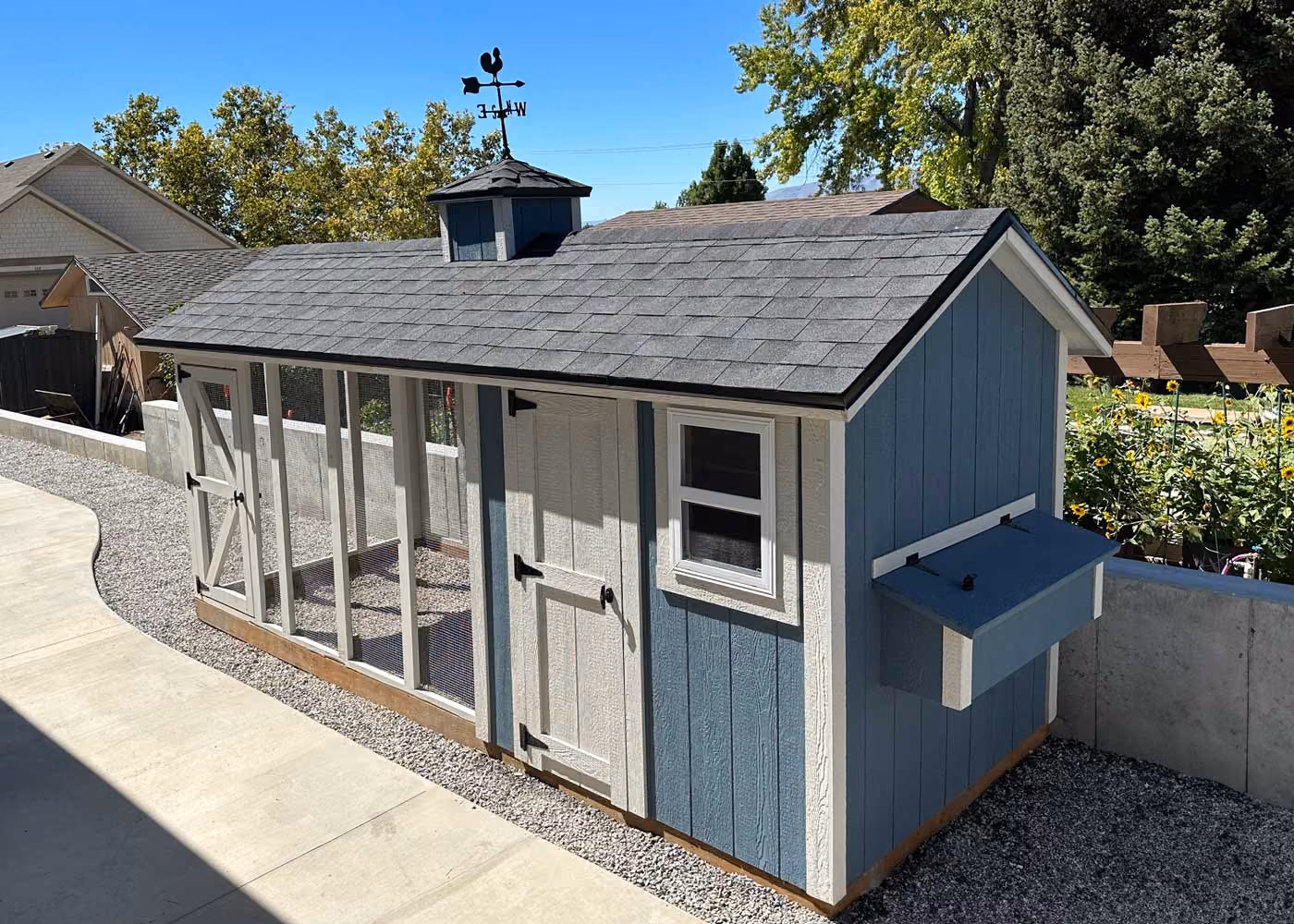Blue and white chicken coop with an enclosed run, cupola, and weather vane
