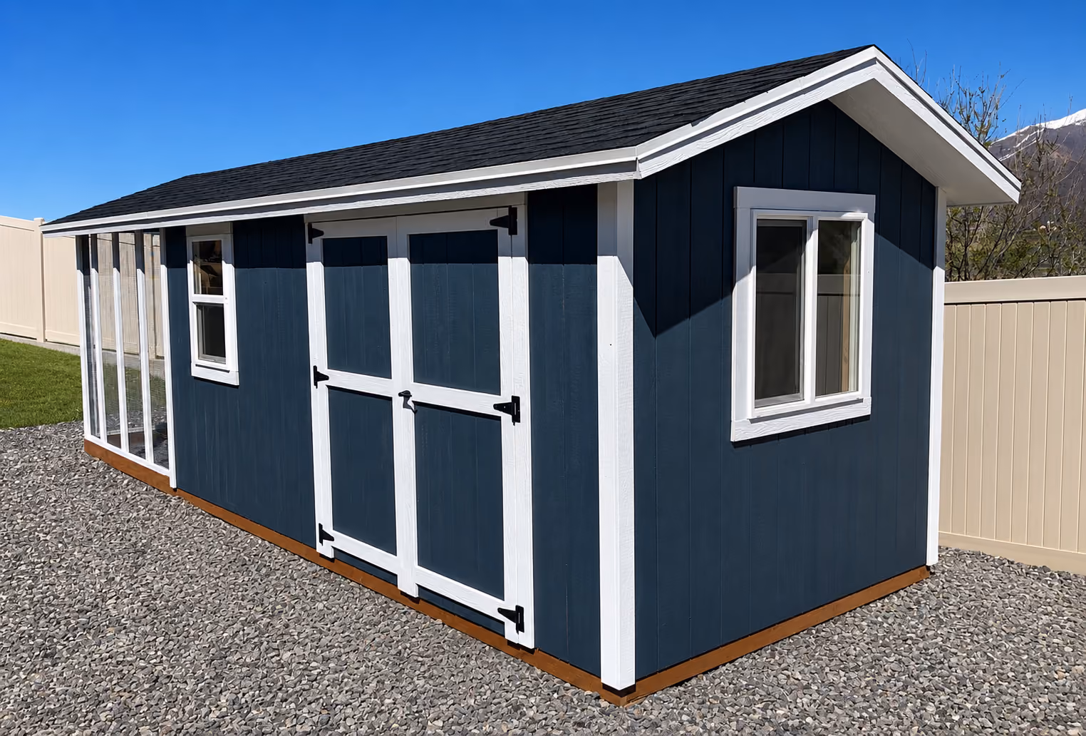Blue custom chicken coop and shed combination with an enclosed run in a gravel backyard with mountain views.