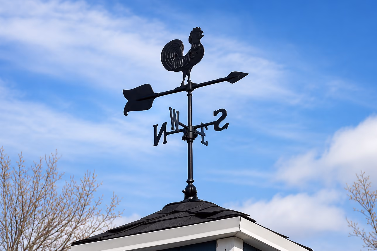 Rooster weather vane mounted on a chicken coop cupola against a blue sky.