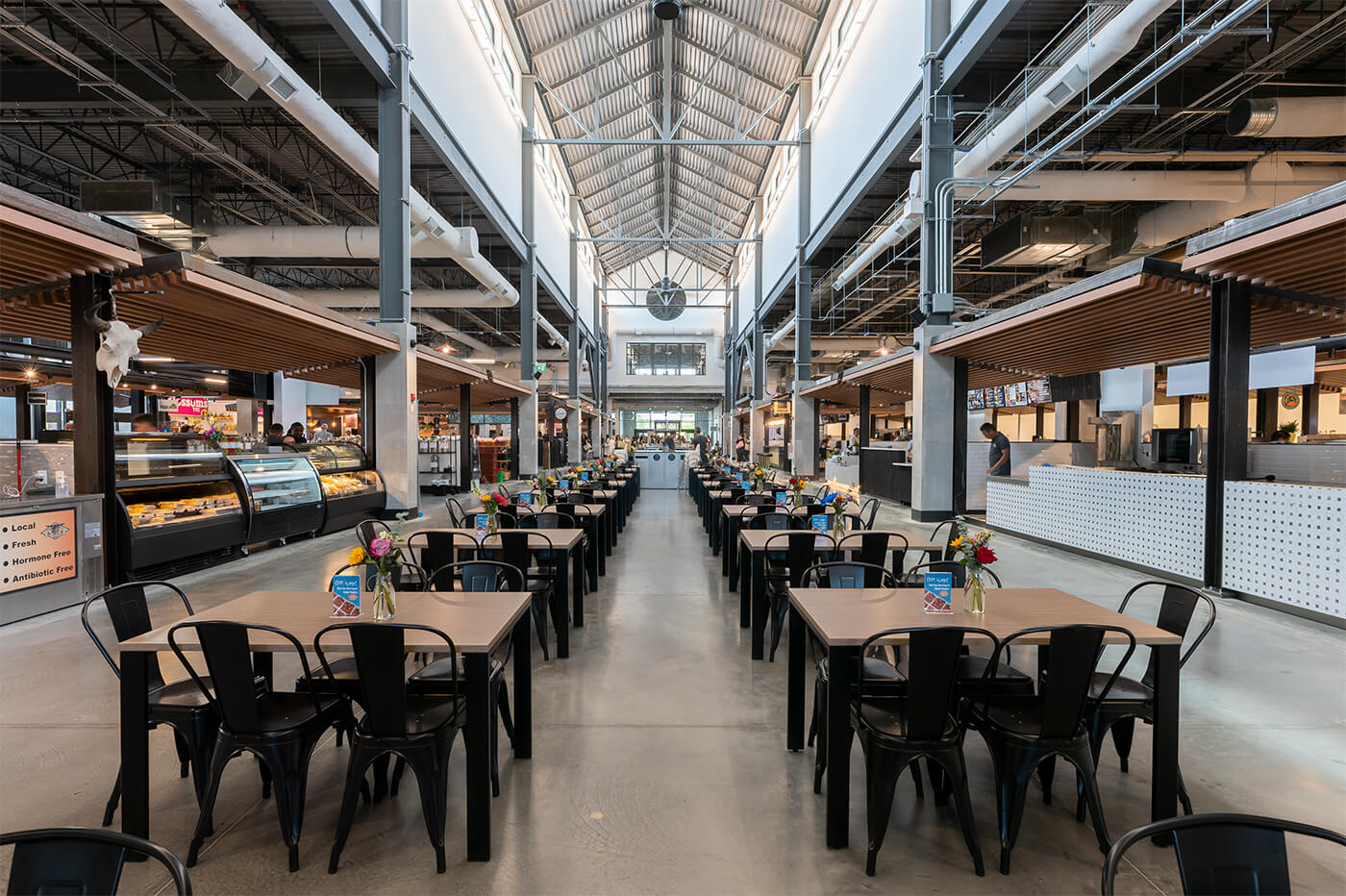 Interior of a modern Calgary market hall with high vaulted ceiling, industrial beams, and rows of communal tables—showcasing the city’s vibrant, design-forward business culture.
