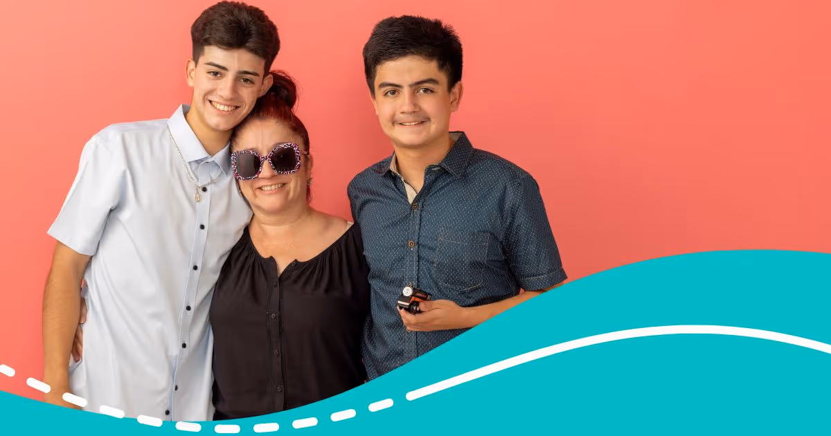 Three happy people posing in front of a coral background with a teal wave graphic at the bottom; a woman wearing dark sunglasses stands between two smiling young men.