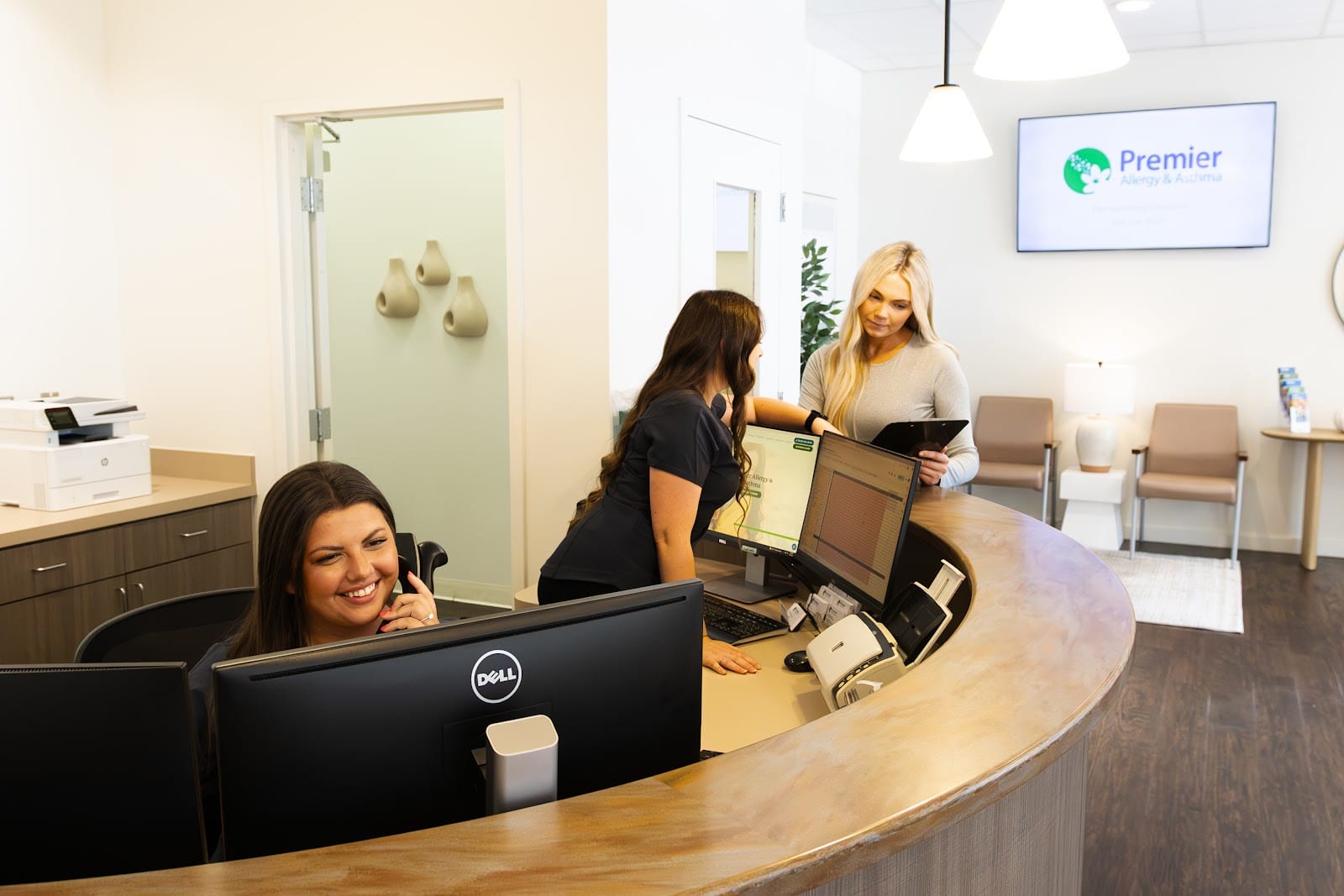 Three women interact at a curved reception desk, with one staff member talking on the phone.