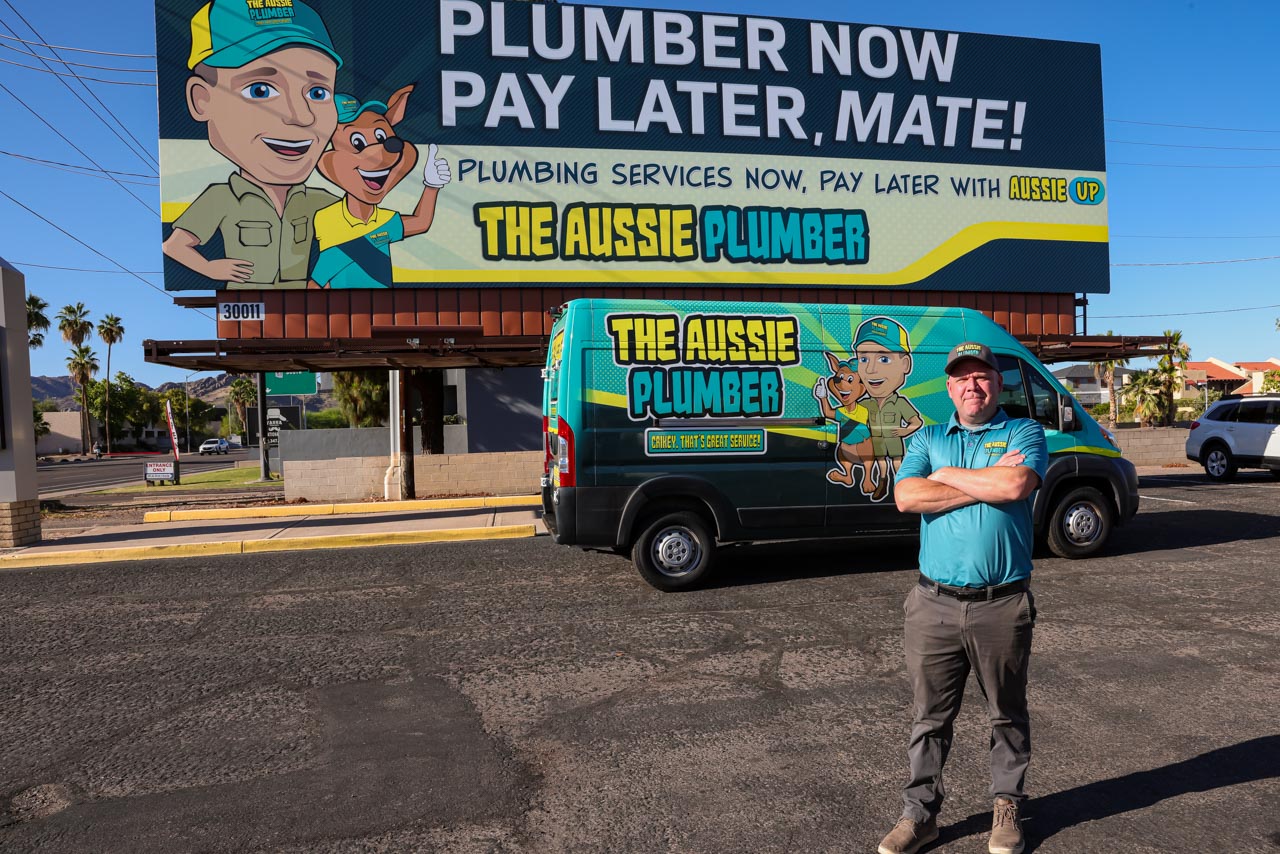 The Aussie Plumber founder James Hill stands in front of his "His Plumber Now, Pay Later" billboard in Phoenix, Arizona