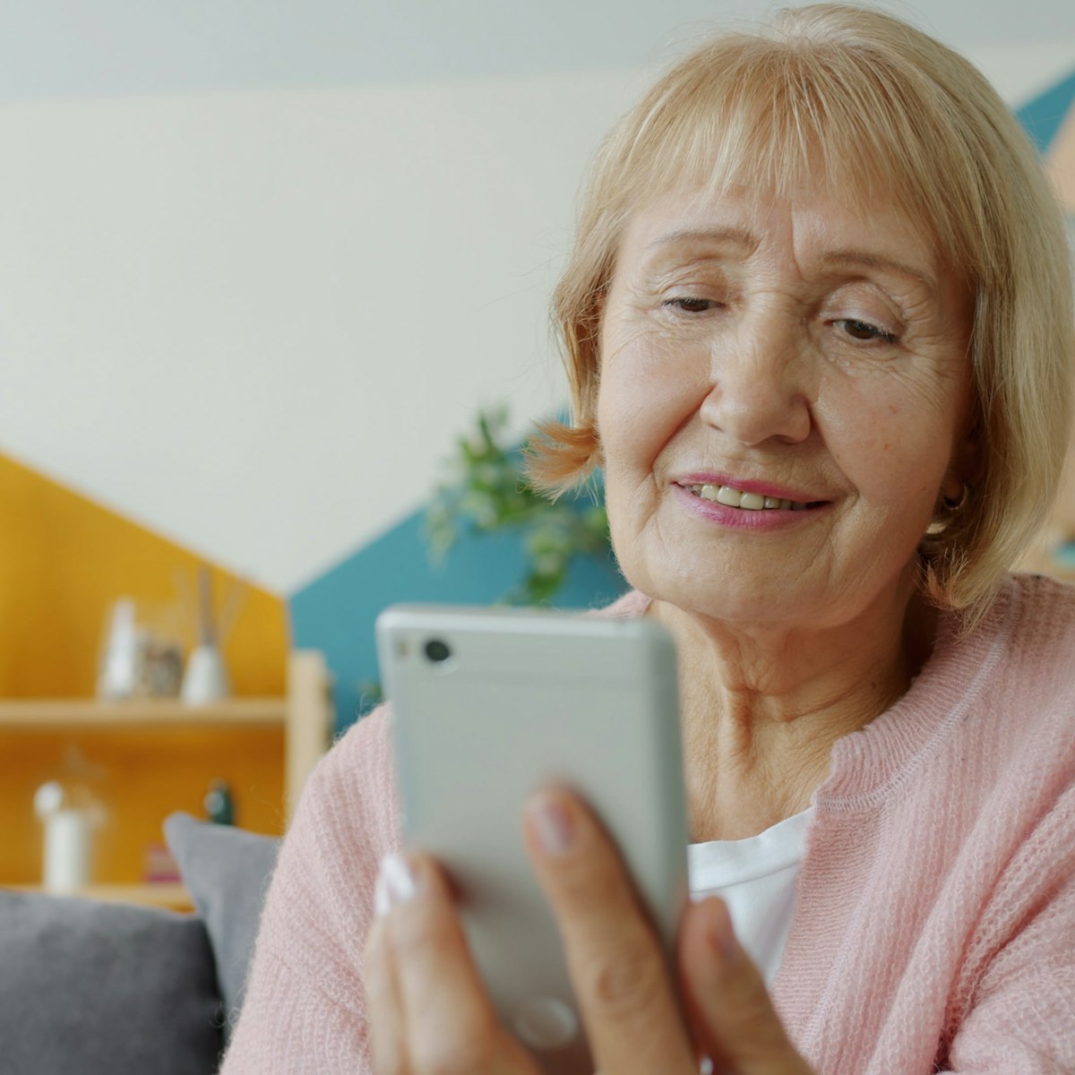 Patient at home smiling while reading a follow-up message on her phone after hospital discharge