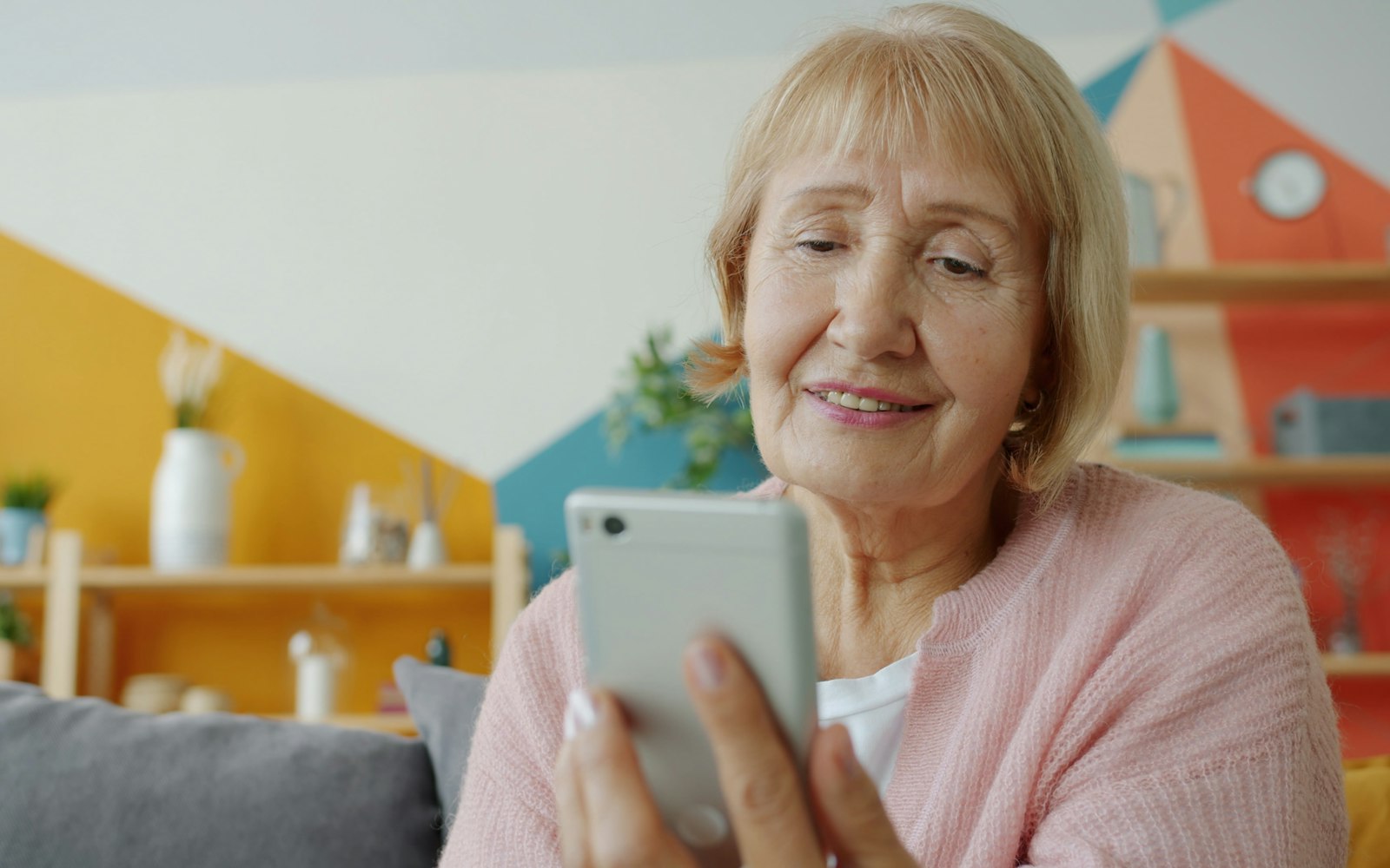 Patient at home smiling while reading a follow-up message on her phone after hospital discharge