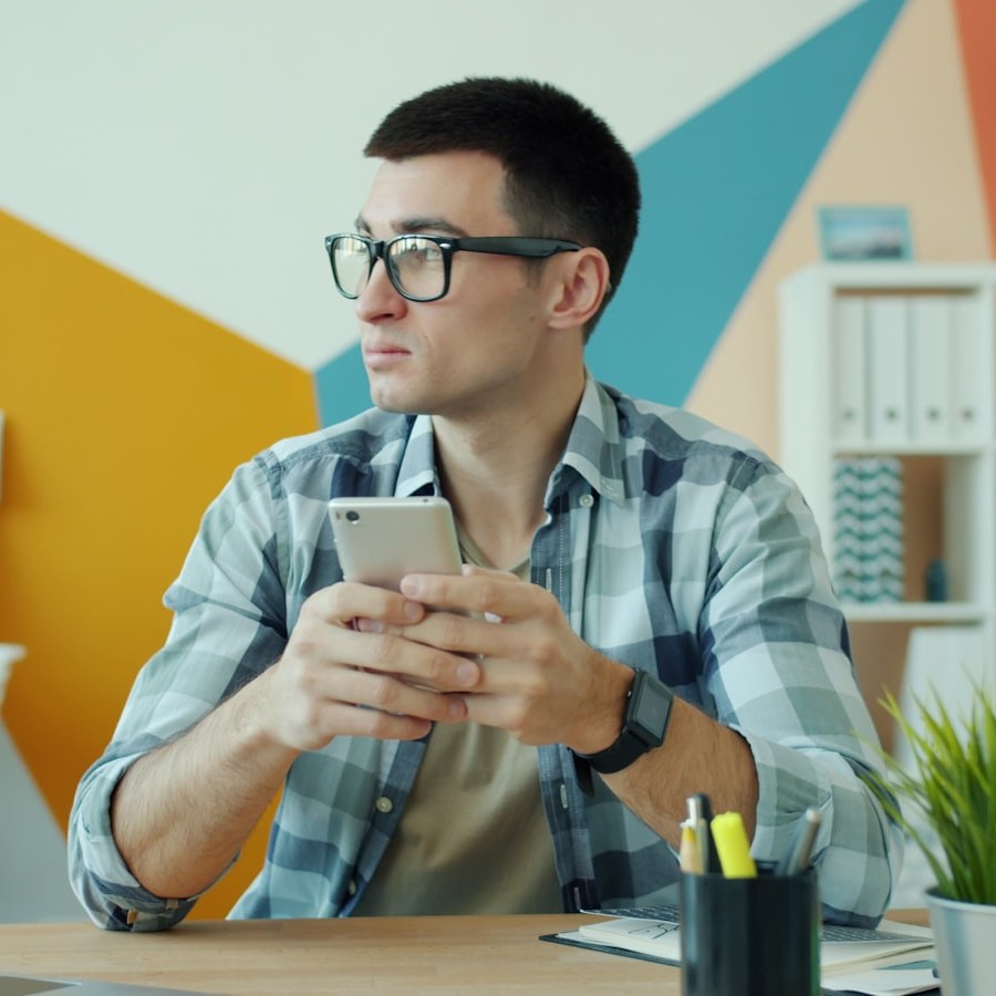 Man with glasses holding smartphone at desk