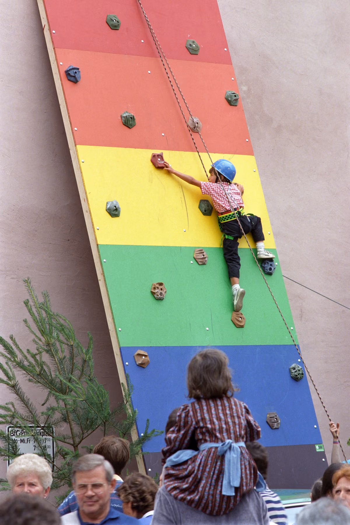 Kind klettert gesichert an einer bunten Kletterwand beim Bürgerfest 1988.