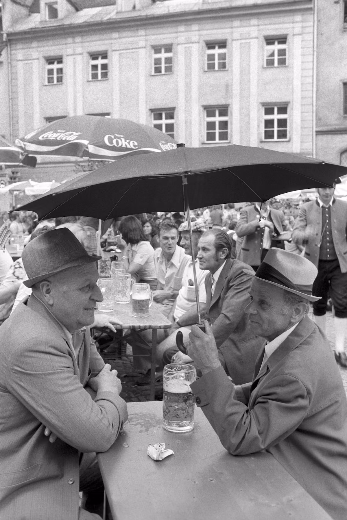 Zwei Männer mit Bierkrügen unter einem Regenschirm beim Regensburger Bürgerfest 1975.