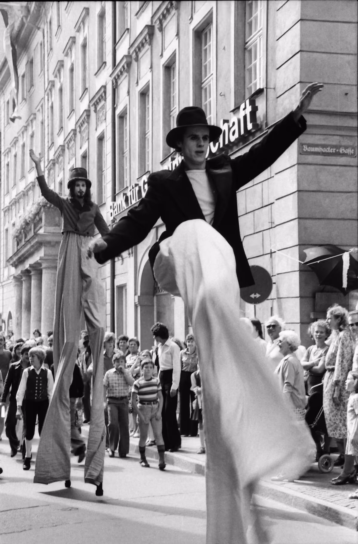 Zwei Stelzenläufer ziehen durch eine von Publikum gesäumte Straße beim Regensburger Bürgerfest 1979.