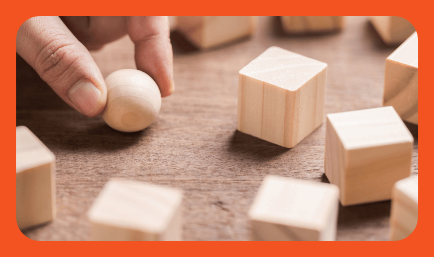 Closeup of a hand holding a round wooden sphere among an array of square wooden blocks, to illustrate the concept of brand metrics