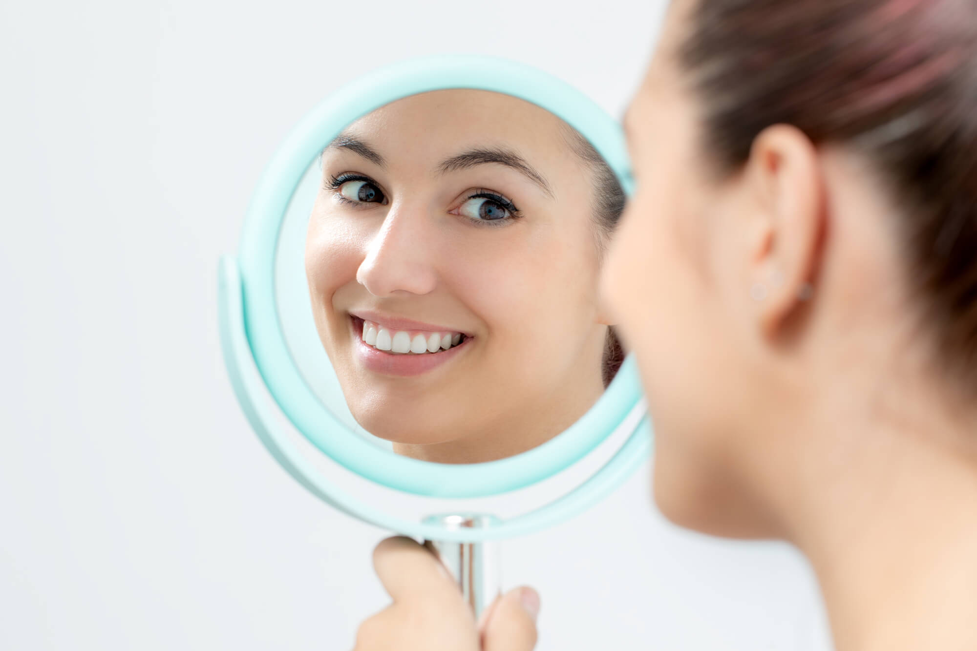 Woman looking at her teeth in the mirror after visiting a cosmetic dentist in Pompano Beach