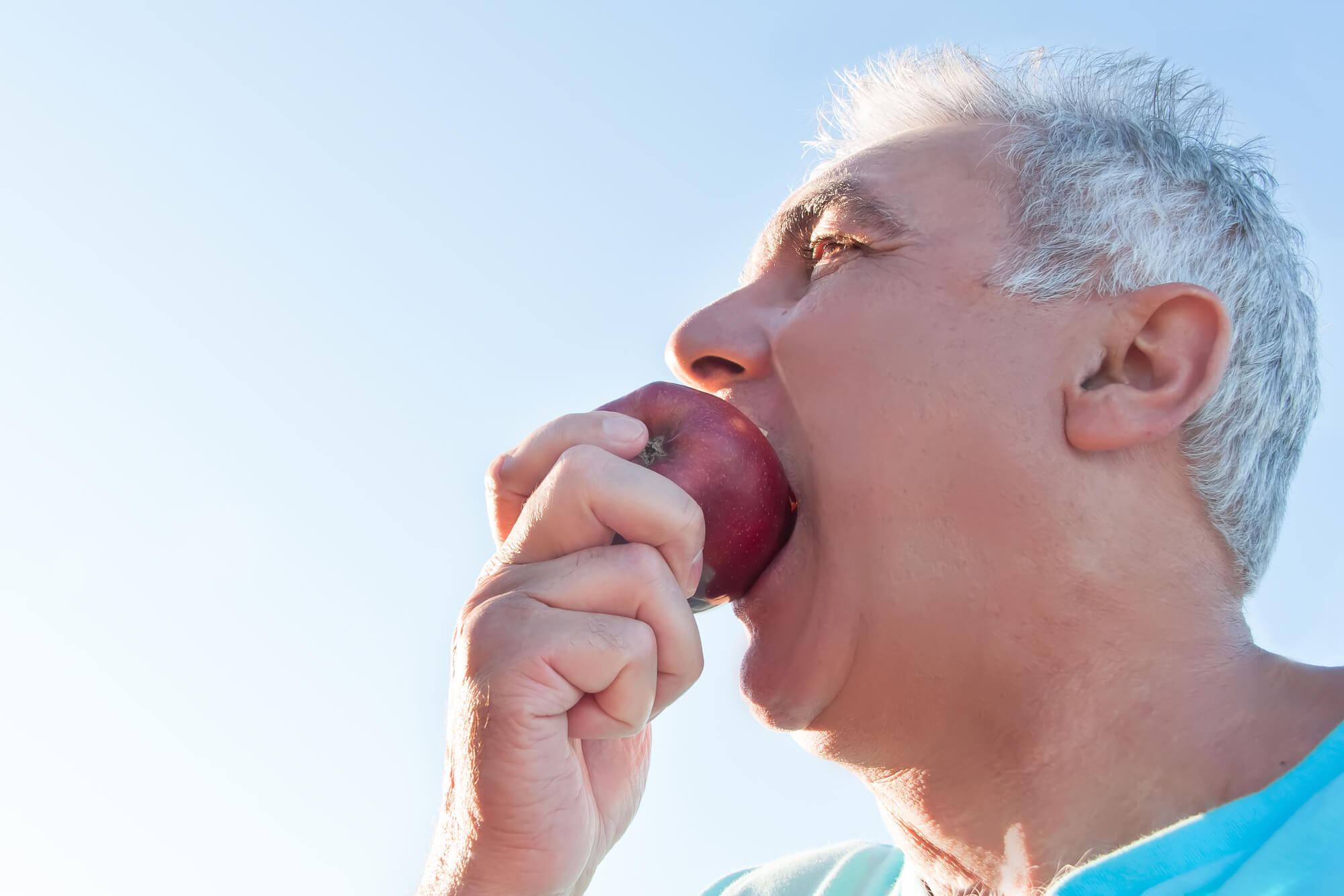 old man biting on an apple with his new dental implants in 33062