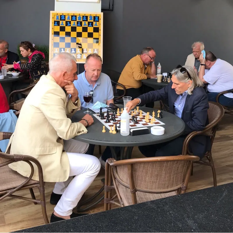 Three older male persons in a restaurant are looking at a chessboard