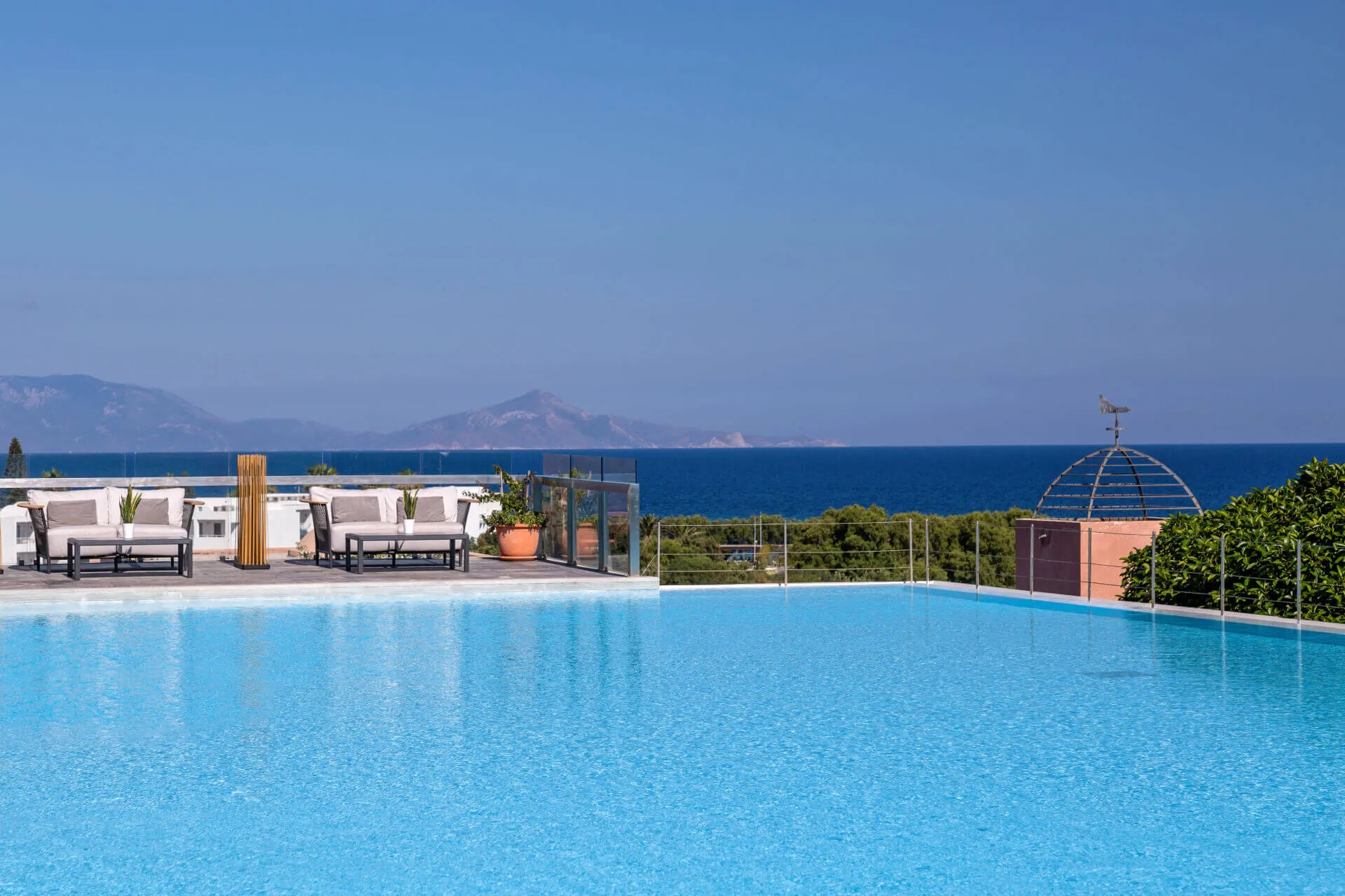 Large pool with seating, in the background mountains and the Mediterranean Sea
