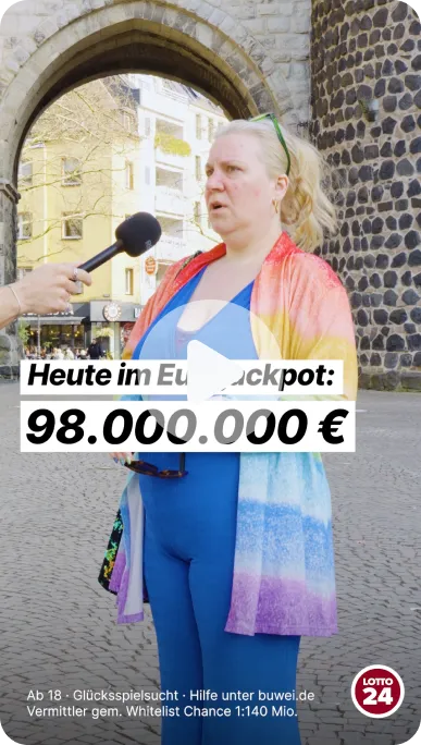 Frau in bunter Jacke und blauer Kleidung spricht vor alten Steinbögen in der Stadt, während ein Mikrofon ihr zugehalten wird. Text zeigt Eurojackpot-Gewinn von 98 Millionen Euro.