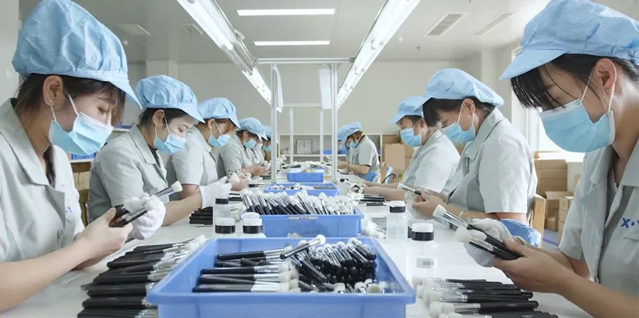 Workers performing final quality inspection and packaging of makeup brushes in a clean factory environment.