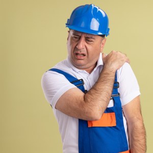 Worker in a hard hat holding an injured shoulder