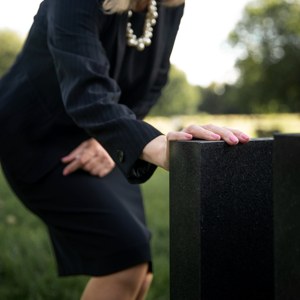 A mourner resting a hand on a headstone