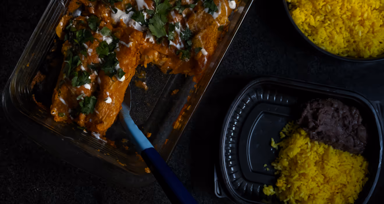 Tray of cheese enchiladas with red sauce and crema, plated with Spanish rice and black beans for corporate catering delivery