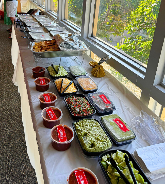 Corporate catering taco bar with trays of chips, salsa, guacamole, cheese, and toppings.